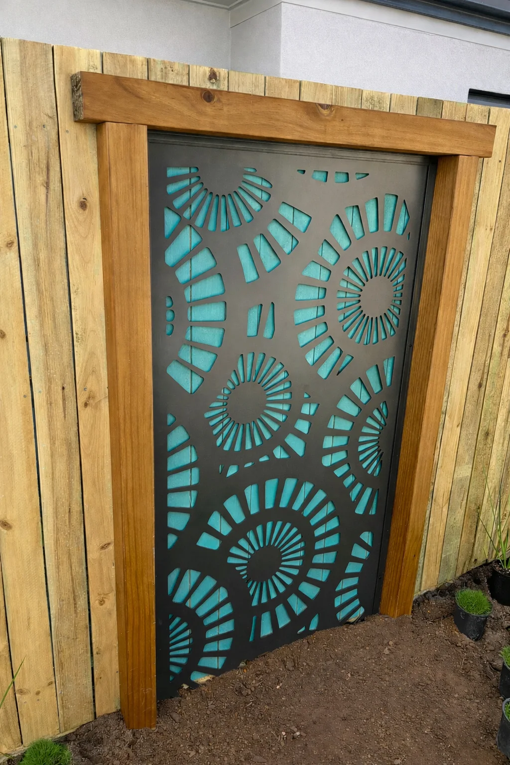 Black laser-cut feature screen with teal backing and stained timber frame installed on an Innisfail fence